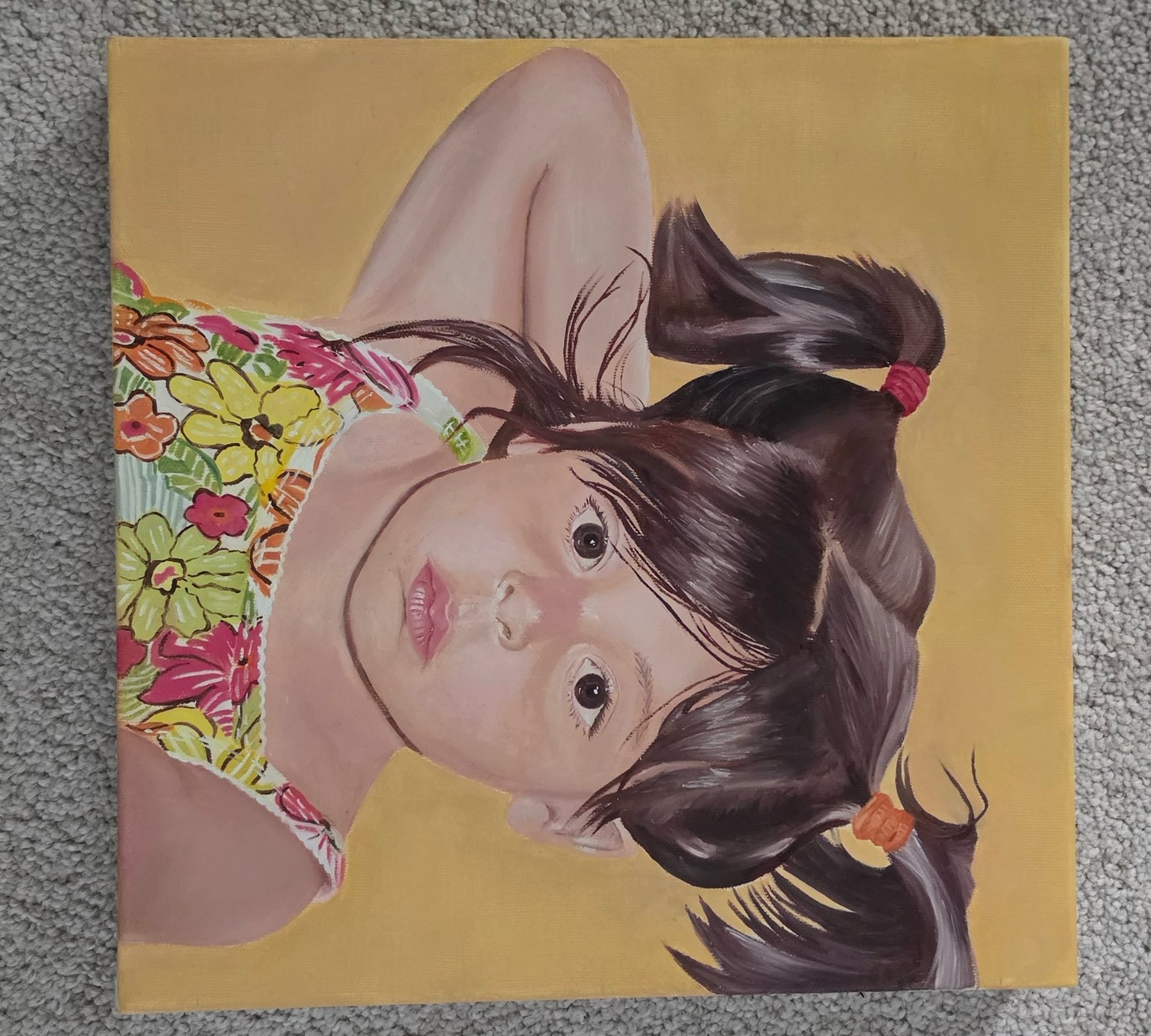 Portrait of a young girl with pigtails in a floral top, lying on a warm yellow background.